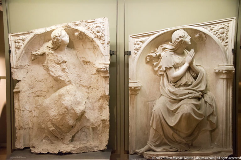 Stone relief of a seated or kneeling woman in profile with hands raised in prayer beneath an arched niche.