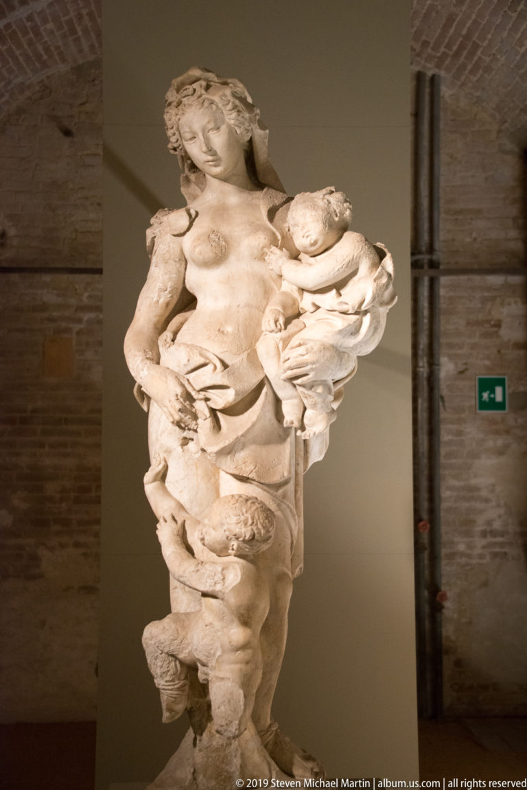 Standing stone Madonna holding the Christ Child, with intact upper figures and a heavily damaged lower section.