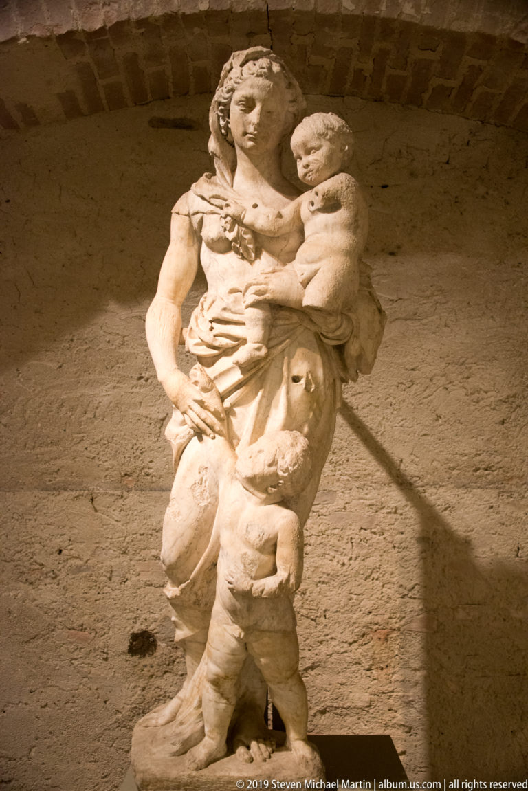 Stone sculpture of the standing Virgin holding the Christ Child, with deeply folded drapery and a worn surface.