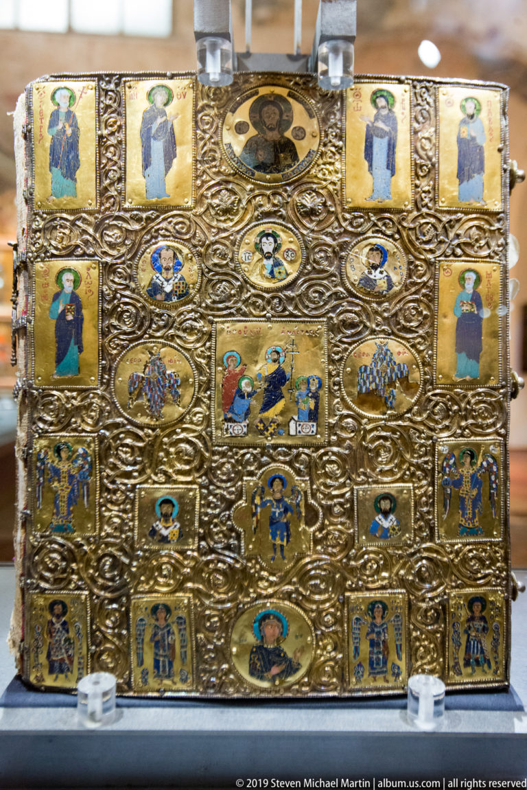 Rectangular gilded liturgical object covered with embossed sacred figures, enamel-like plaques, medallions, and scrolling ornament.