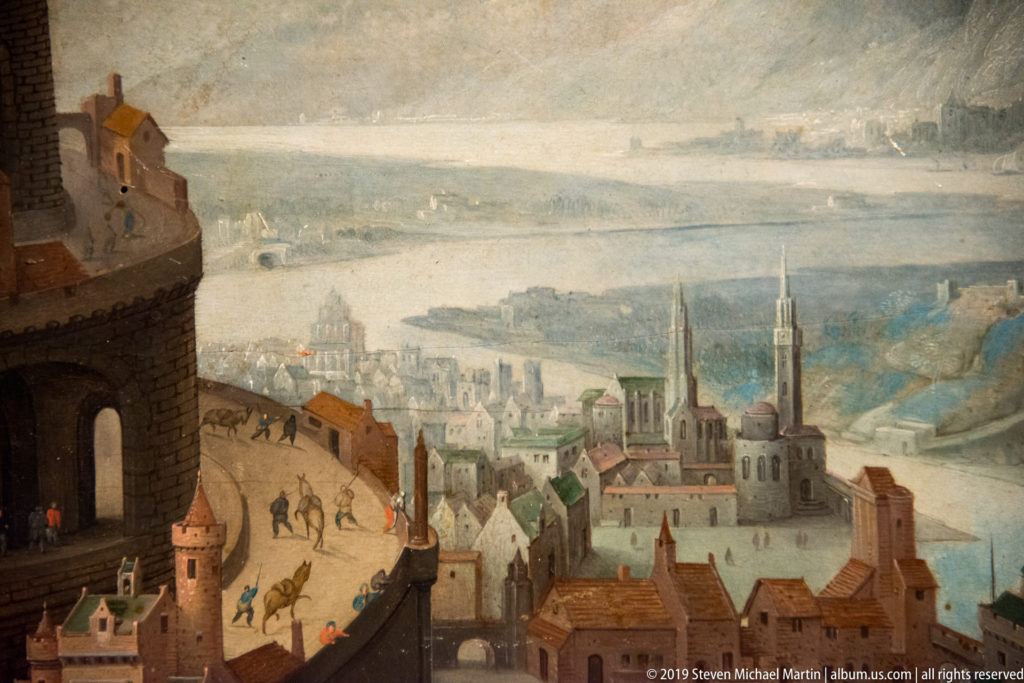Painted fortified city with twin church spires, steep streets, tiny figures, water, and distant hills.
