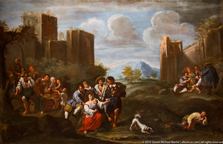 Travelers rest on a road between large ruined towers, with mountains and open countryside beyond.
