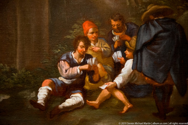 Men in travel clothes gather around a seated figure while one tends his bare foot.