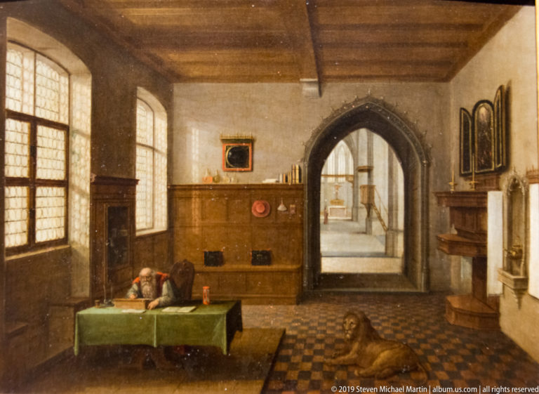 Painted room with leaded windows, green-covered table, timber paneling, tiled floor, and pointed doorway.