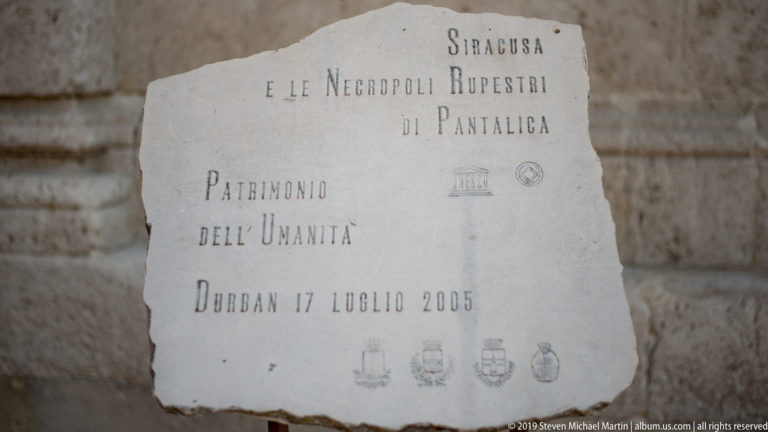 Stone UNESCO plaque reading “Siracusa e le Necropoli Rupestri di Pantalica,” with World Heritage and civic emblems.