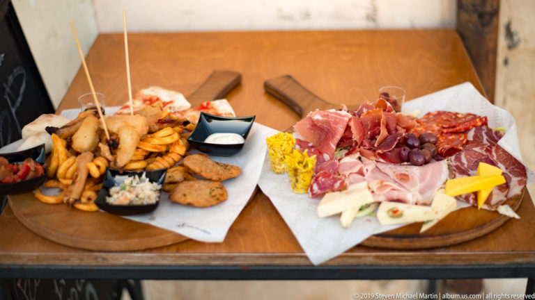 Two wooden platters with fried seafood, cured meats, cheeses, olives, grapes, sauces, and assorted savory bites.