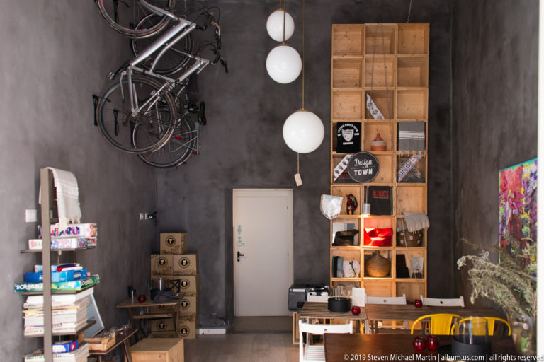 Dark contemporary interior with bicycles hung high on a wall, globe lights, wooden shelving, books, and colorful furnishings.