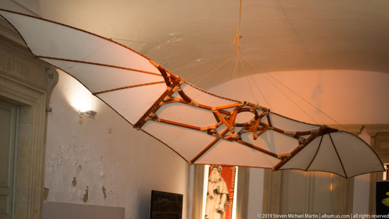Large suspended winged mechanical model with wooden framework and pale fabric surfaces inside a museum.