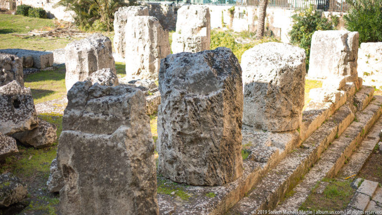 Cluster of weathered limestone column stumps aligned within the sunlit Temple of Apollo archaeological area.