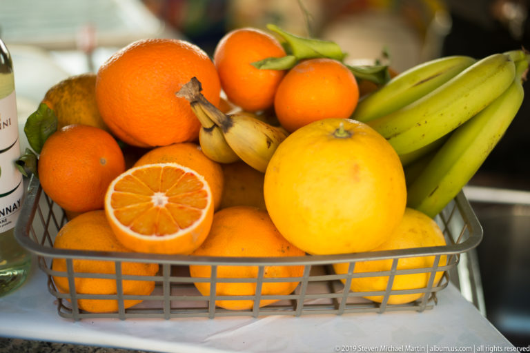 Basket filled with oranges, halved citrus, bananas, and a large yellow fruit at a food stand.