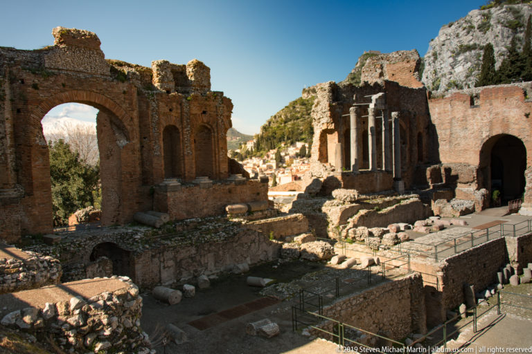 Brick arches, standing columns, stone foundations, and scattered architectural fragments within the Ancient Theatre of Taormina.