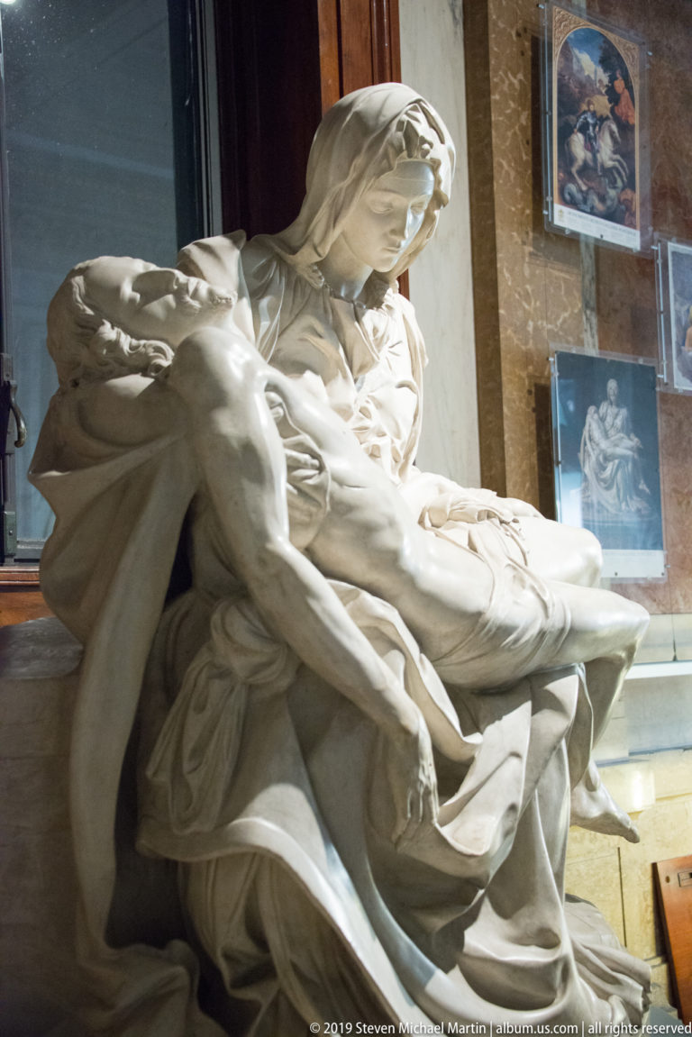 White marble Pietà with the Virgin bending over Christ's body across her lap amid deeply carved drapery.