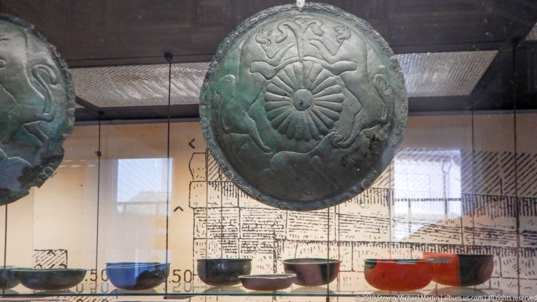 Large green-patinated bronze shield with a radiating central rosette and concentric bands of stylized animal and scrolling motifs.