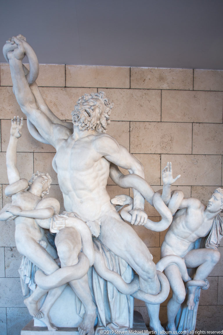 Marble Laocoön group with a bearded central man and two youths struggling against large serpents wrapped around their bodies.