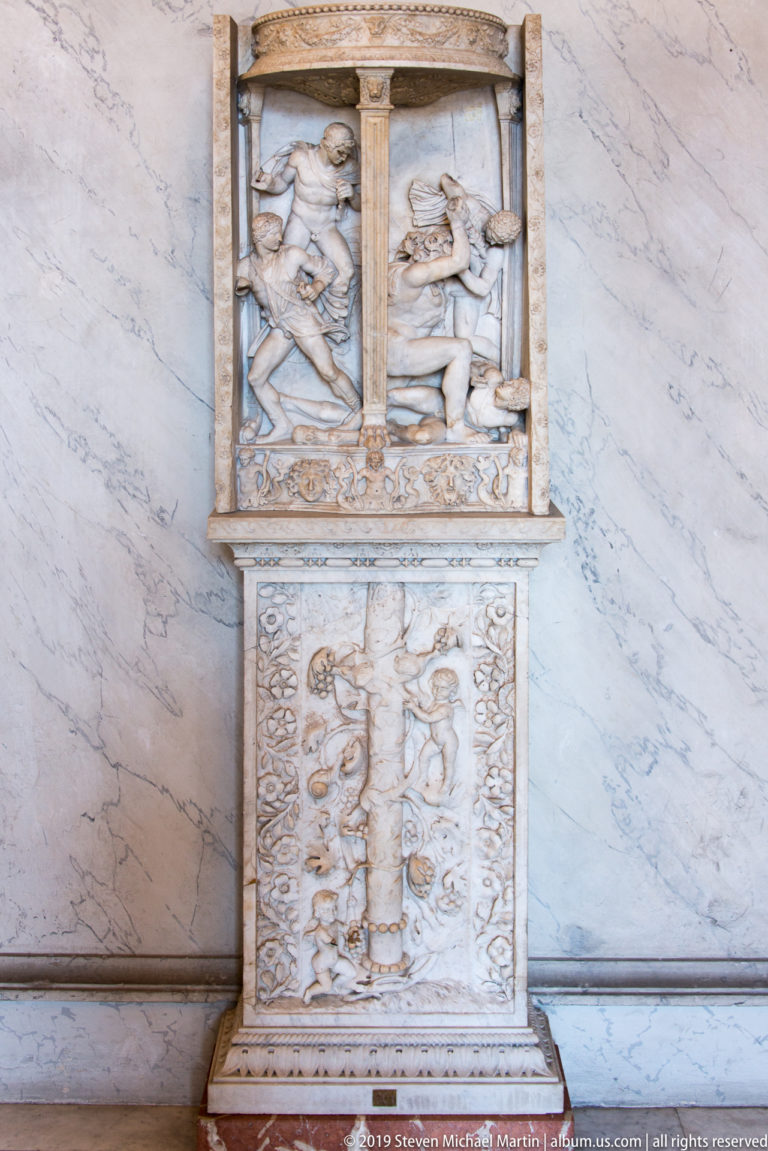 Pale marble relief monument with two upper figural panels divided by columns and a larger crowded narrative relief below.