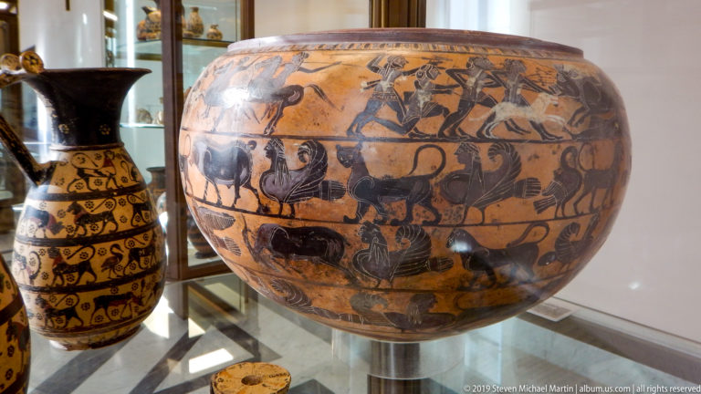 Broad orange ceramic bowl with black painted horsemen, lions, birds, and other animals arranged in horizontal friezes.