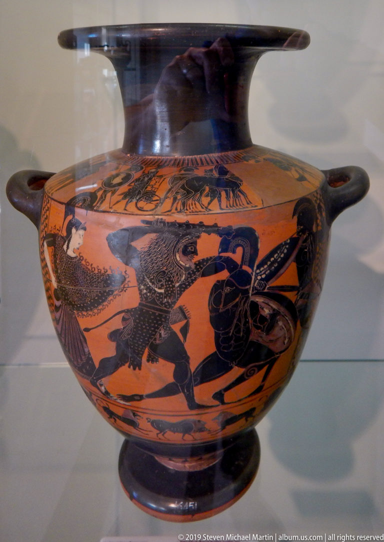 Ancient orange-red ceramic vessel with black painted figures, animals, decorative bands, projecting handles, and a broad rounded body.