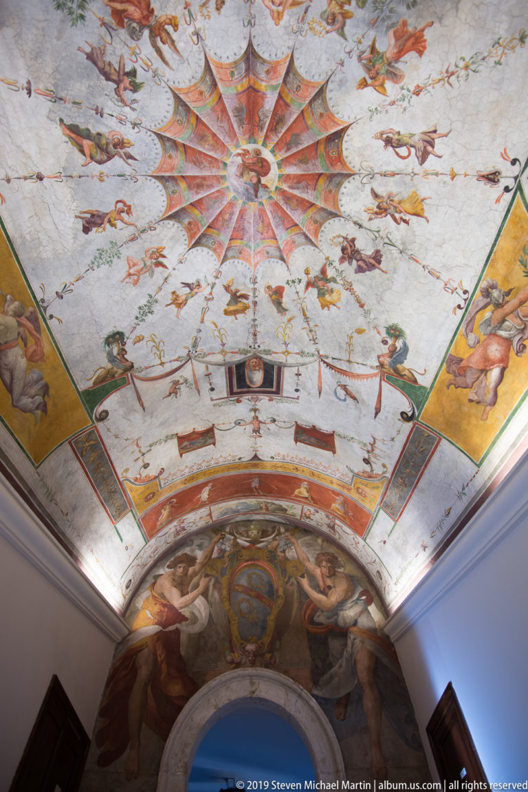 Painted vault with a central multicolored starburst, surrounding figures and animals, and a richly decorated lunette below.