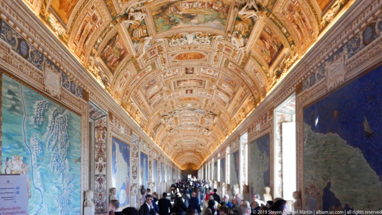 Crowded Gallery of Maps with monumental wall maps, tall windows, visitors, and a richly gilded barrel-vaulted ceiling.