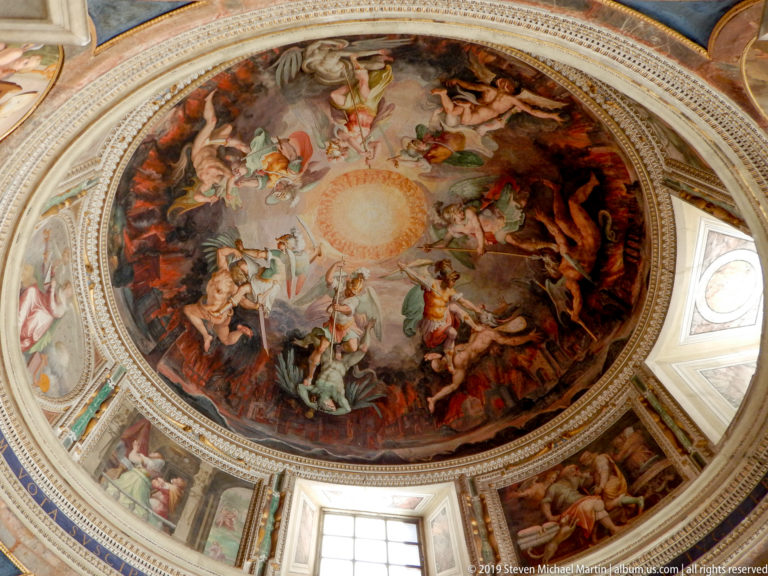 Circular dome fresco with many figures swirling around a radiant central light, surrounded by windows and painted architectural decoration.