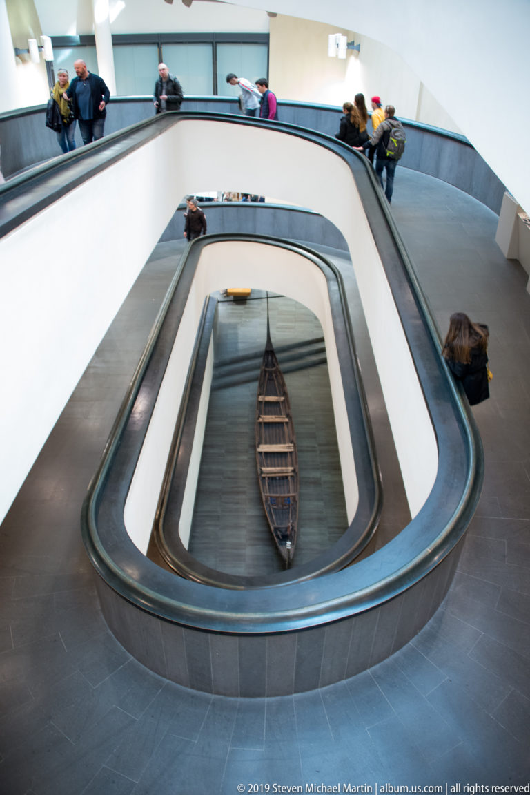 Giuseppe Momo's double-helix staircase viewed from above, with dark railings, white concentric ramps, visitors, and a boat-shaped display below.