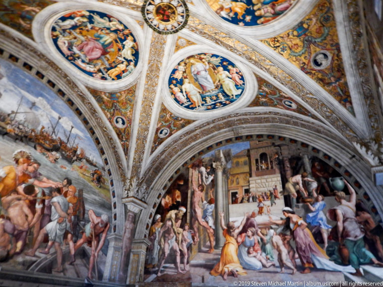 Corner of a frescoed Vatican room with a harbor battle, crowded dramatic wall scene, and circular ceiling paintings above.