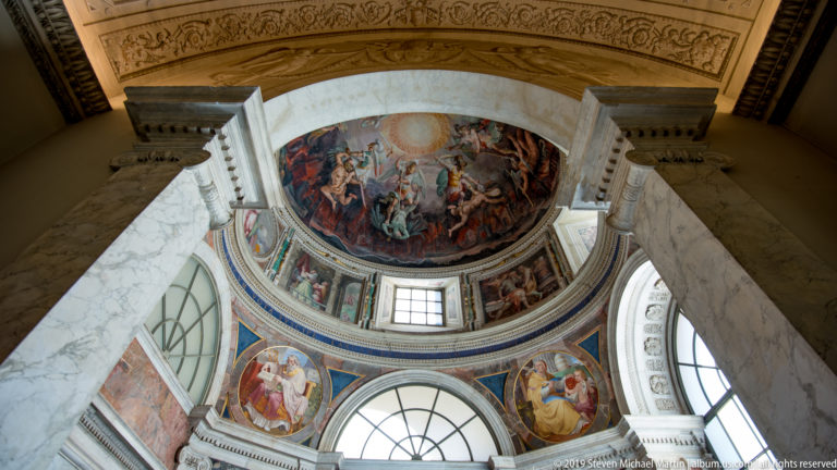Frescoed cupola with radiant center and swirling figures, framed by pale marble piers, arches, windows, and smaller roundels.