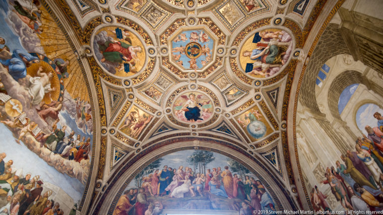 Ornate Raphael Rooms vault with circular figurative medallions, gilded geometric framing, and large frescoes continuing down the walls.