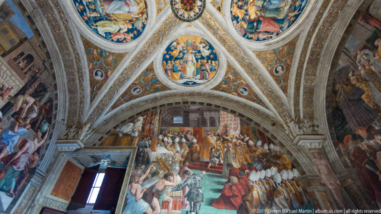 Frescoed cross-vault above a large ceremonial wall scene crowded with richly dressed figures in a Vatican room.