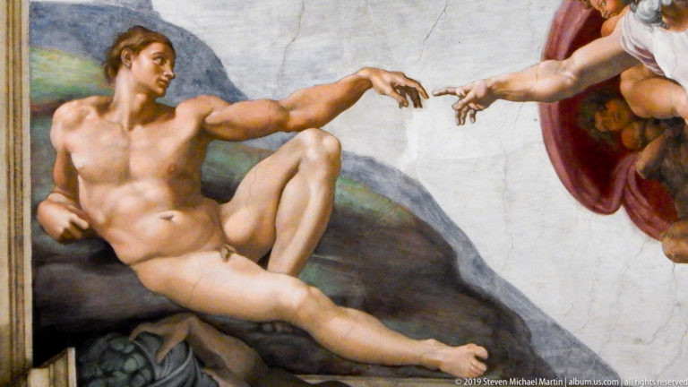 Close detail of Michelangelo's Creation of Adam showing reclining Adam extending his hand toward God's approaching fingers.
