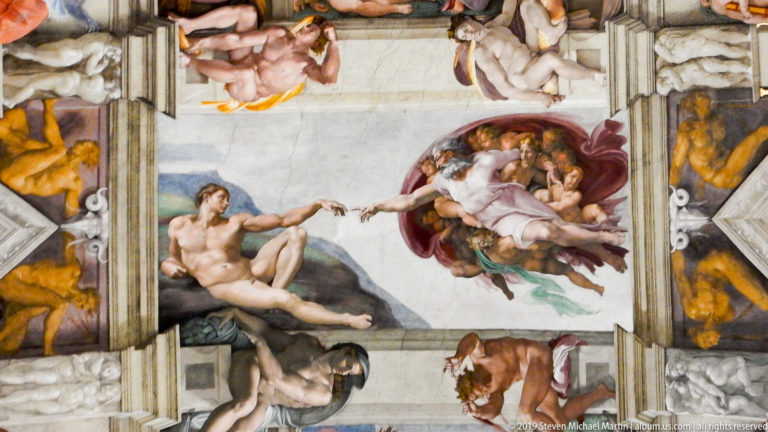 Wide ceiling view of Michelangelo's Creation of Adam, with reclining Adam, God reaching toward him, and surrounding painted figures.