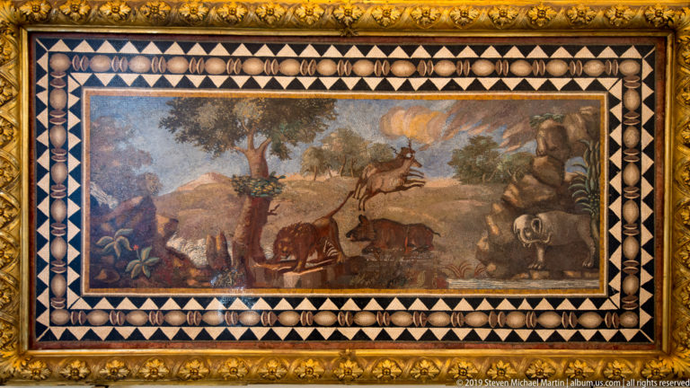 Rectangular mosaic of deer, cattle, and other animals in a wooded landscape, surrounded by a black-and-white geometric border.