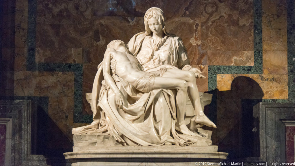 Michelangelo’s marble Pietà with the Virgin Mary supporting the dead Christ against a dark, veined stone wall.
