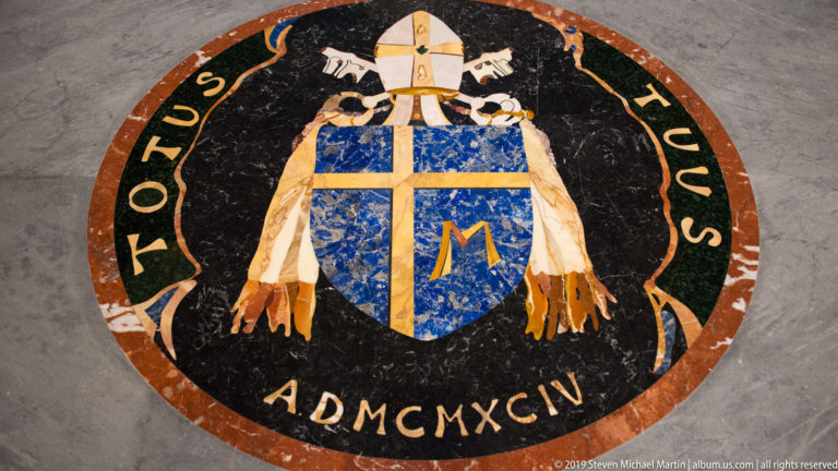 Circular marble floor inlay with papal arms, white mitre, crossed keys, blue shield, TOTUS TUUS inscription, and AD MCMXCIV date.