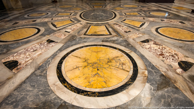 Close view of geometric marble pavement with large yellow circles, black borders, gray stone, and radiating multicolored panels.