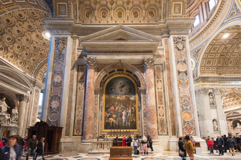 Large chapel altar with an arched sacred image, polychrome marble framing, gilded ceiling, and visitors gathered below.