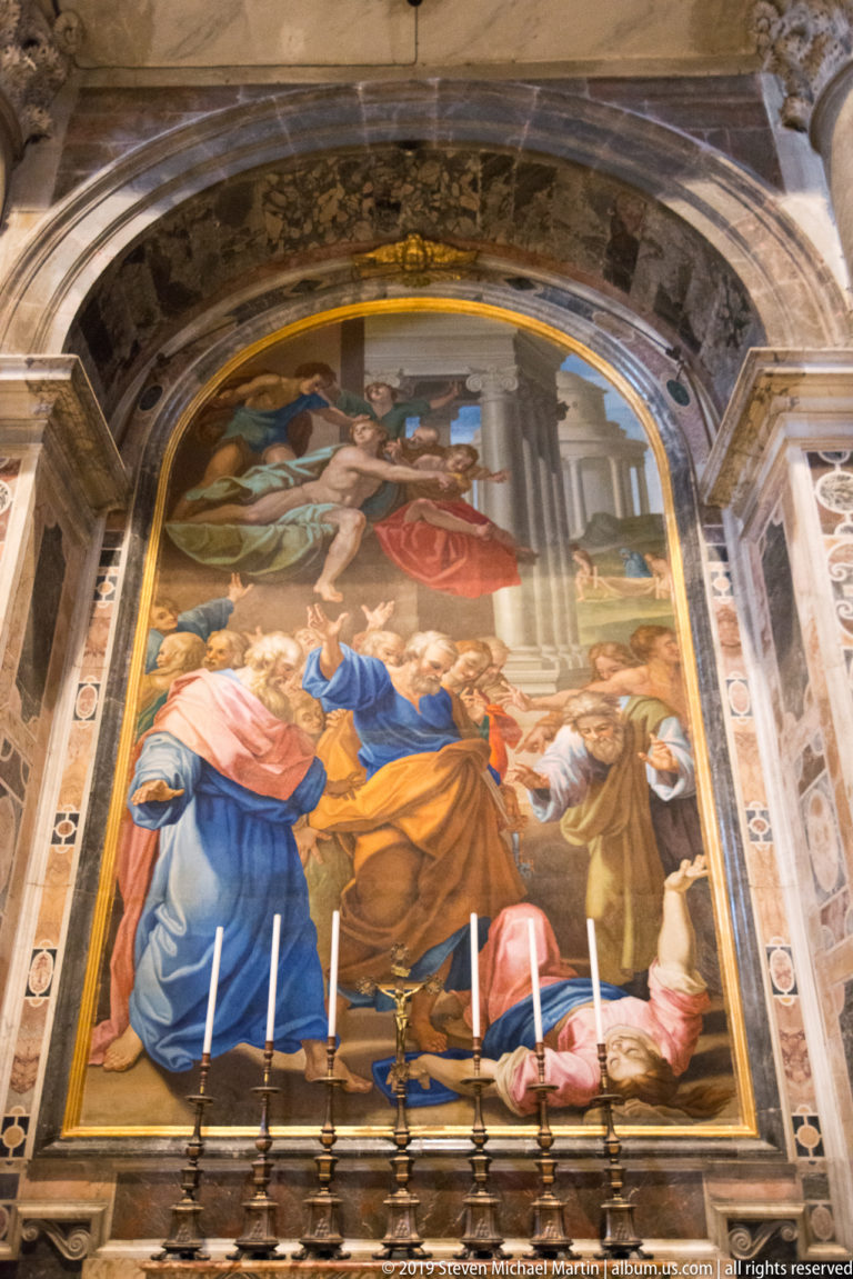 Large arched sacred image with many robed figures above an altar lined with tall candlesticks and framed by colored marble.