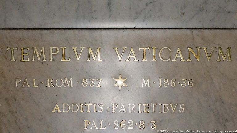 Gold Latin lettering reading TEMPIVM VATICANVM with numerical measurements set into a gray marble slab.