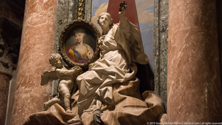 Papal monument with seated marble pontiff, winged figure, oval portrait medallion, and red marble columns.