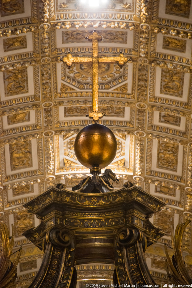 Gilded orb and cross crowning Bernini’s dark bronze baldachin beneath an ornate coffered ceiling.
