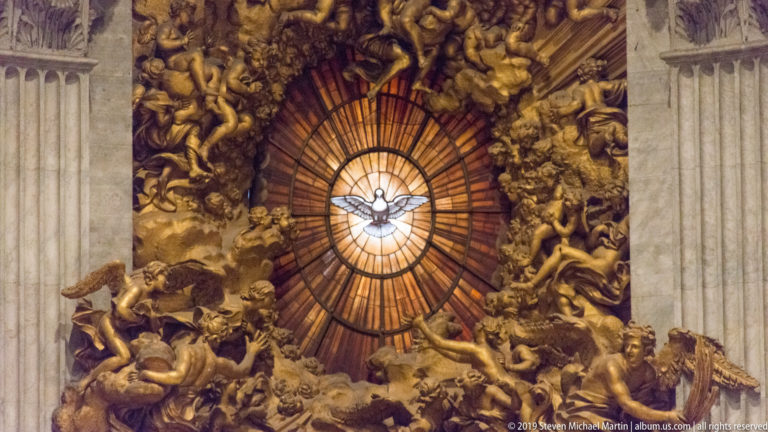 Dove of the Holy Spirit centered in a glowing amber window surrounded by gilded clouds, angels, and rays.