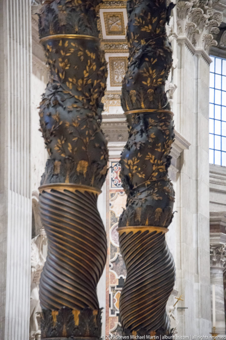 Close view of two twisted bronze columns of Bernini’s baldachin, enriched with gilded foliage and ornament.