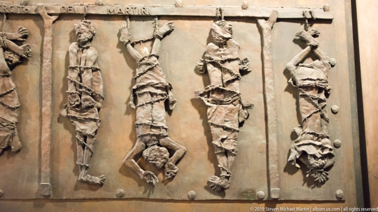 Bronze relief with several bound human figures arranged vertically across large metal panels.