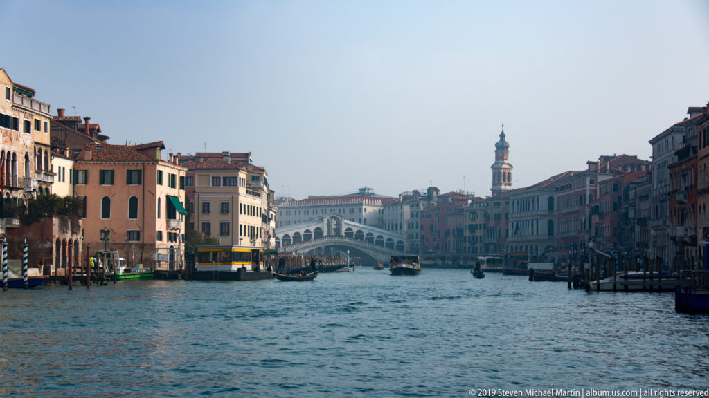 Rialto Bridge spanning the Grand Canal in the distance, framed by waterfront buildings and boats.