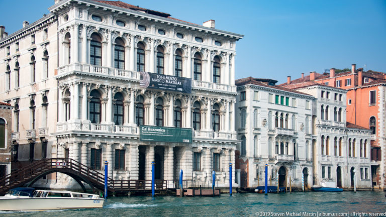 White Baroque façade of Ca’ Rezzonico on the Grand Canal, with an arched footbridge and neighboring palazzi.