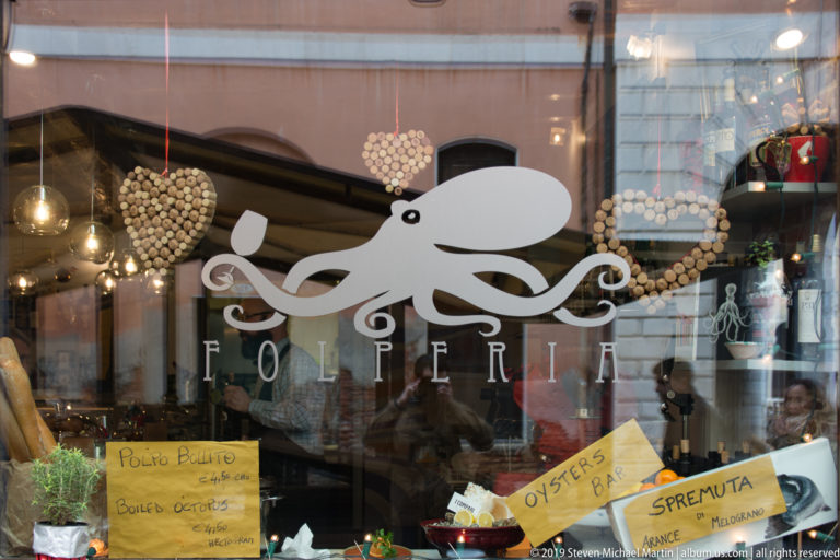 Folperia storefront window with a large white octopus logo and handwritten cards advertising oysters, spritz, and seafood.