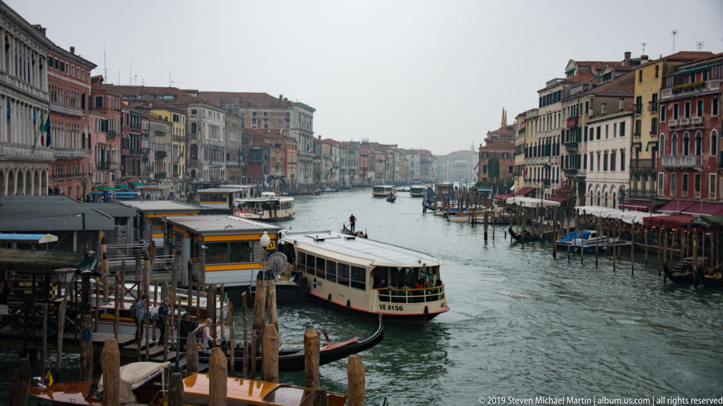 Grand Canal viewed from above with a vaporetto, gondolas, docks, and long rows of historic palazzi.