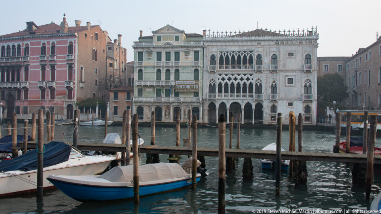 Ca' d'Oro across the Grand Canal behind small covered boats, timber mooring posts, and a low dock.