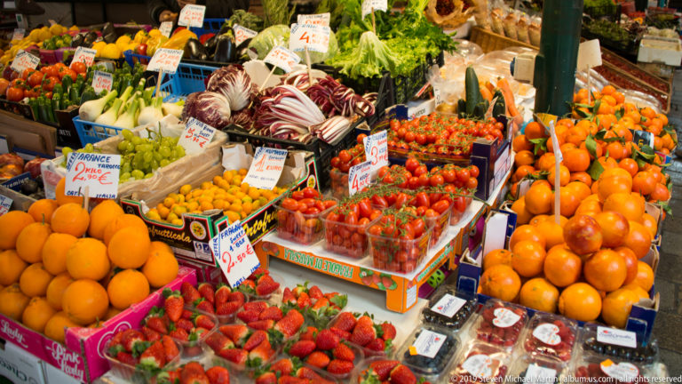 Colorful Rialto produce stall with oranges, strawberries, tomatoes, radicchio, fennel, and handwritten price cards.