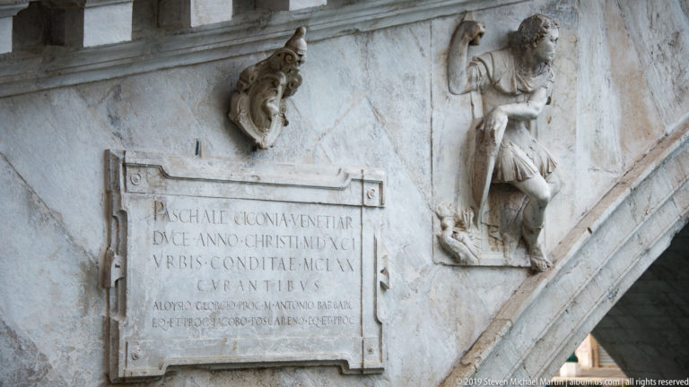 Marble Latin inscription naming Pasquale Cicogna beside carved relief figures on the masonry arch of the Rialto Bridge.